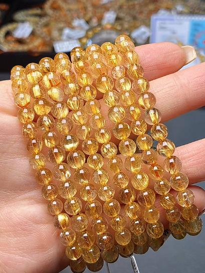 Golden rutilated quartz beads with fine gold needles, held in hand